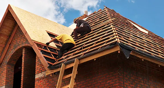 Two workers installing a new roof on a brick house